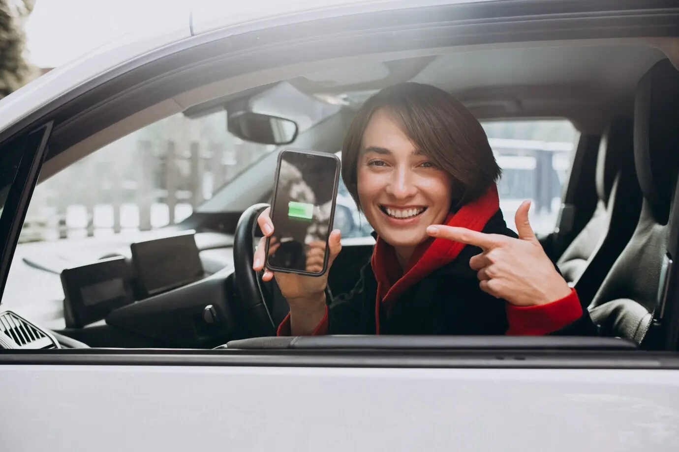 A woman is charging her car while checking the charger on her phone.
